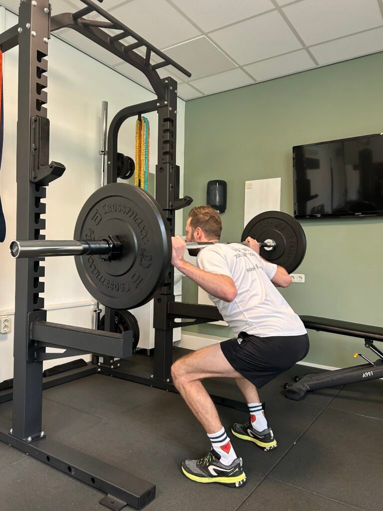 Man voert squat uit met halter in fitness onder begeleiding van personal trainer, krachttraining voor spierbehoud en fitter worden.