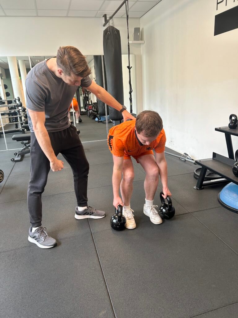 Een man die met Kettle Bel aan het krachttrainen is onder begeleiding van een personal trainer